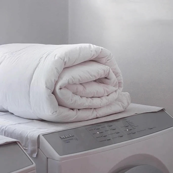 Fluffy white APSMILE duvet resting on top of a washing machine, highlighting its easy-care quality.