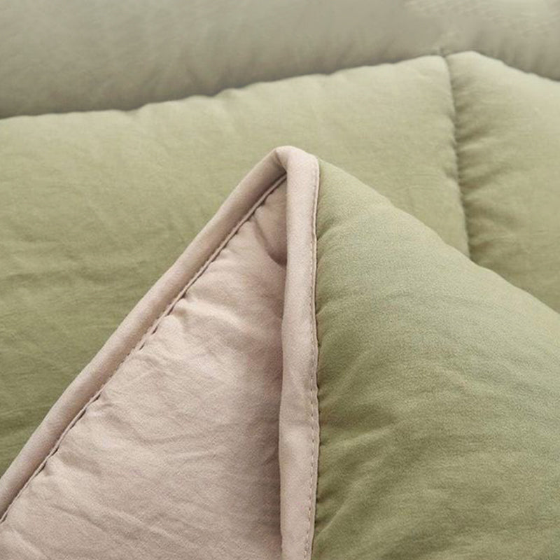 Close-up of a folded sage green and beige quilted blanket.