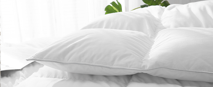 Close-up of fluffy white pillows stacked on a bed, with a blurred background of tropical leaves and a window.