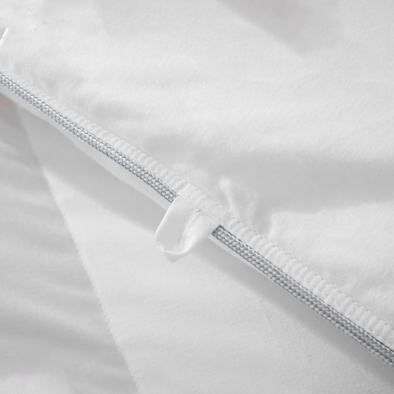 Close-up of a white comforter with silver trim and fabric loops used to secure a duvet cover.
