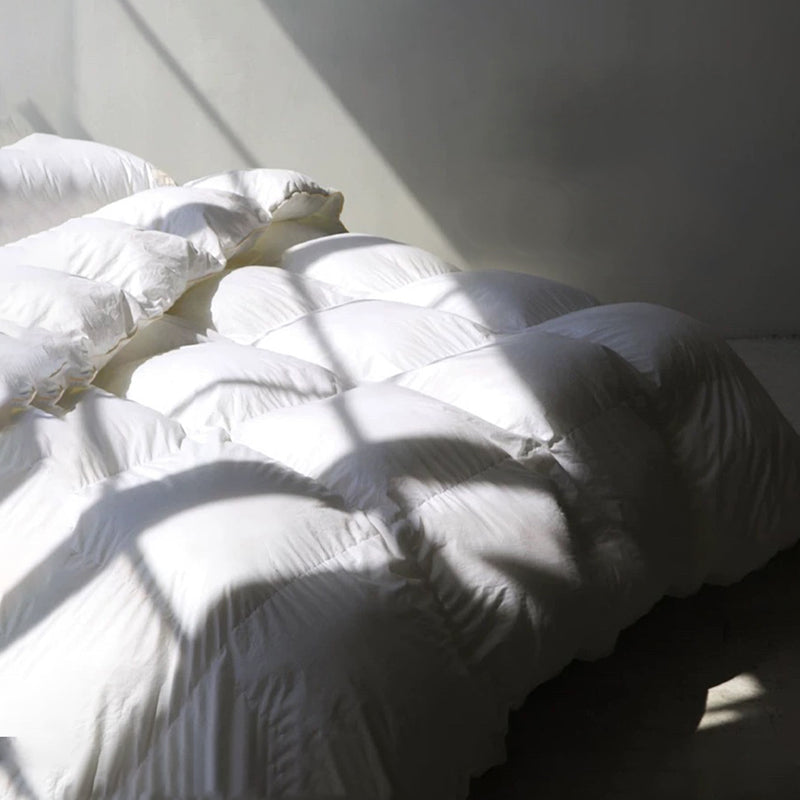Close-up of an APSMILE white down comforter with sunlight and shadows on the wall and comforter.