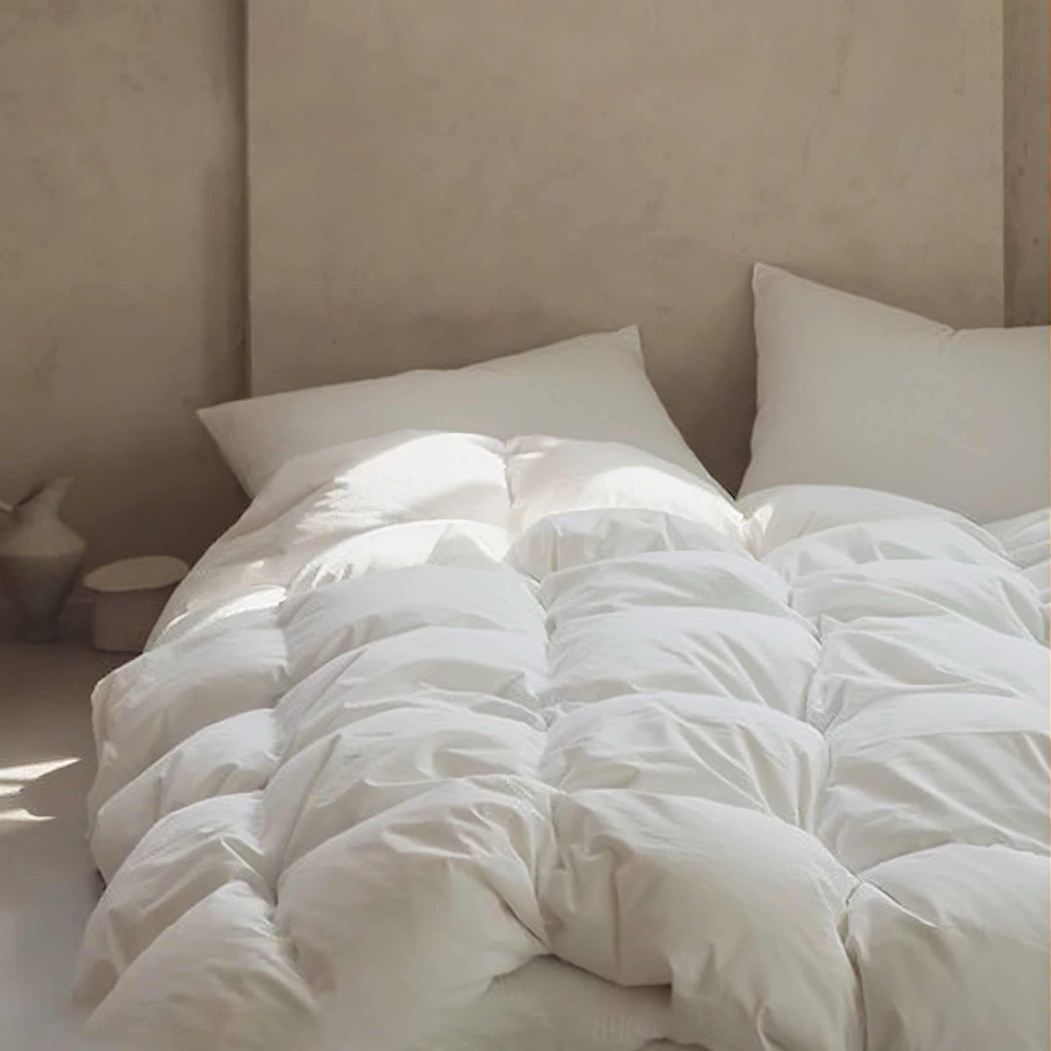 Close-up of a white APSMILE down comforter with a plush, quilted design, displayed against a neutral-toned wall.