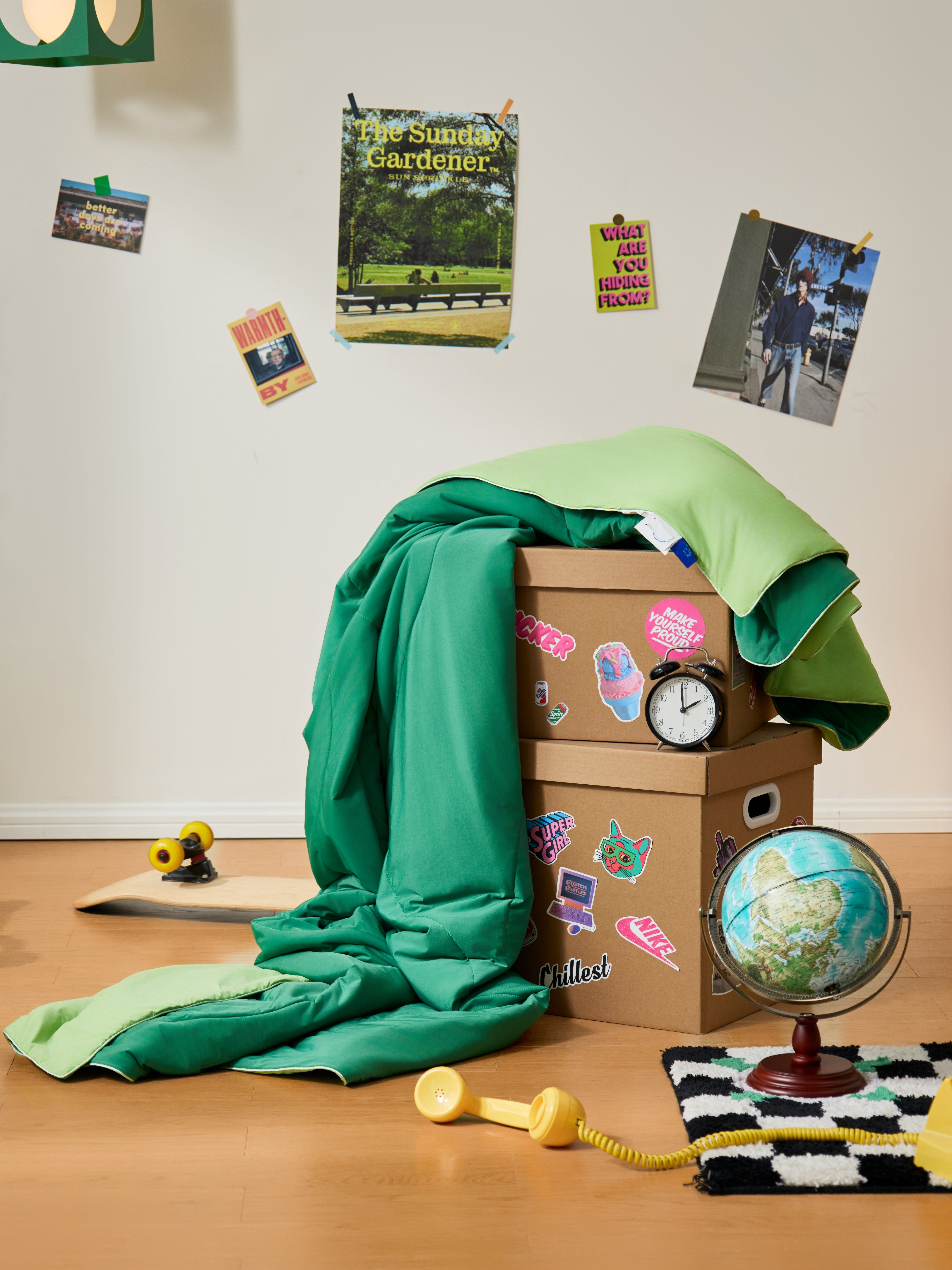 APSMILE's green cooling blanket product display, neatly folded on top of two stacked cardboard boxes with stickers, against a white wall decorated with various postcards and photos.