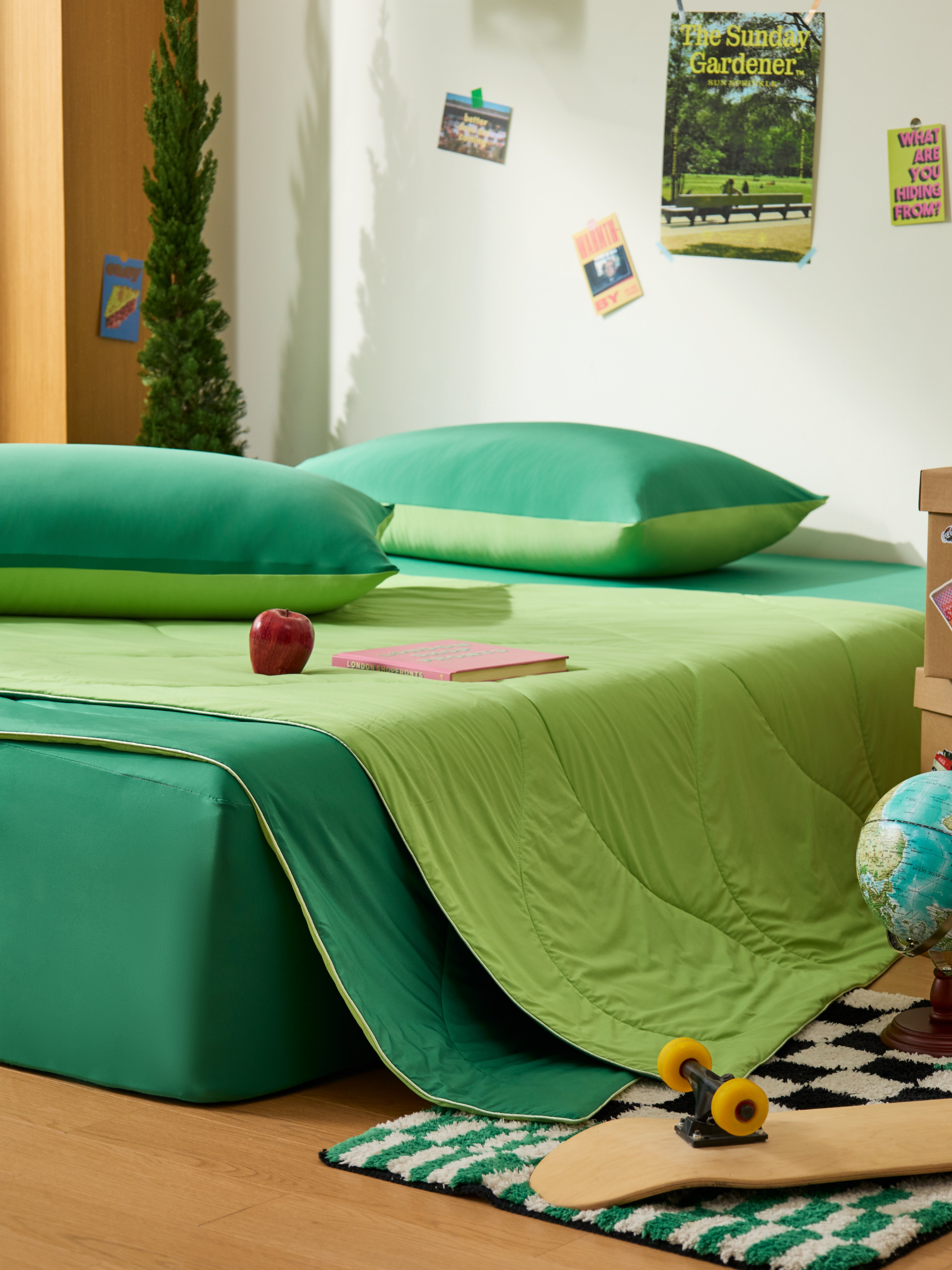 APSMILE cooling blanket in hues of green on a bed, accompanied by coordinating pillows, a book and an apple.