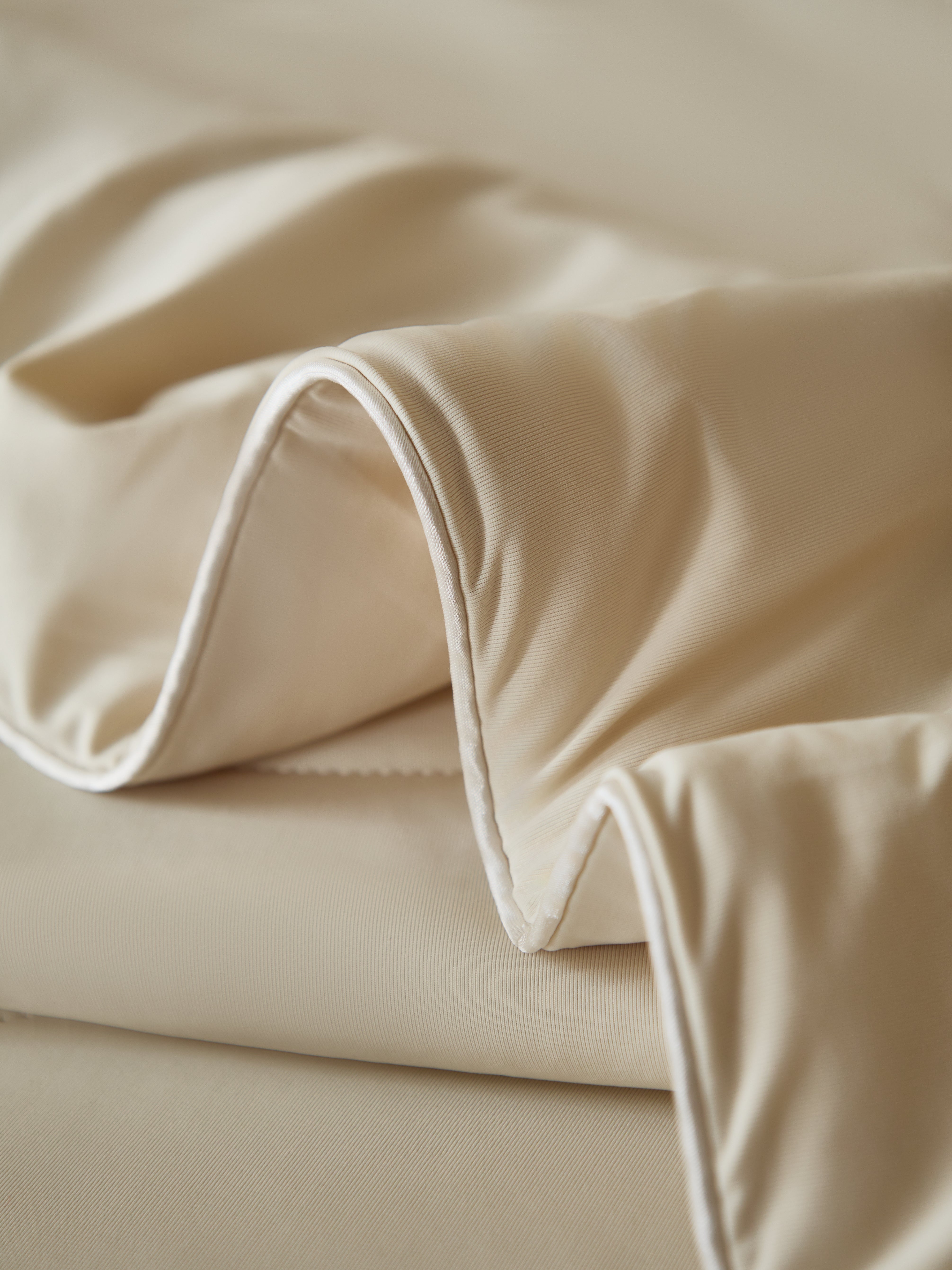 Close-up of folded, cream-colored fabric with a subtle texture and contrasting white piping along the edge.