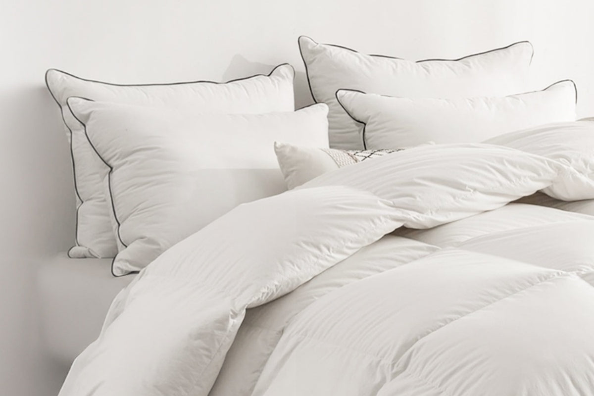 Close-up of plump white APSmile pillows with a fine dark trim on a bed with a white APSmile duvet.