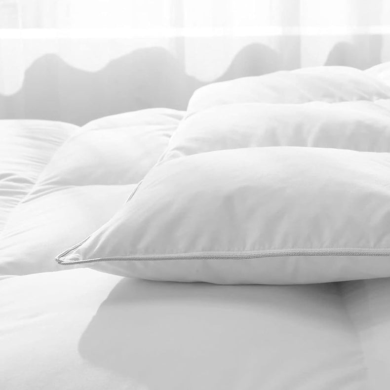  Close-up of a plush, white APSMILE mattress topper with quilted segments and a zippered edge against a light-filled background.  