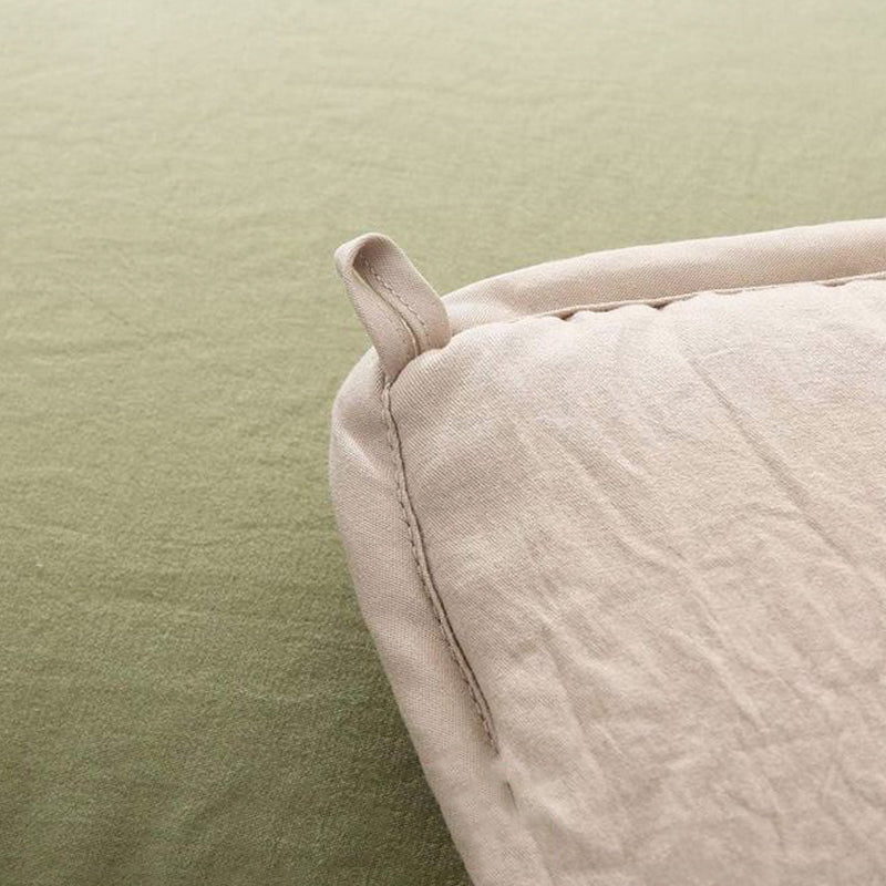 Close-up of a beige linen pillow with a hanging loop placed on a light green textured surface.