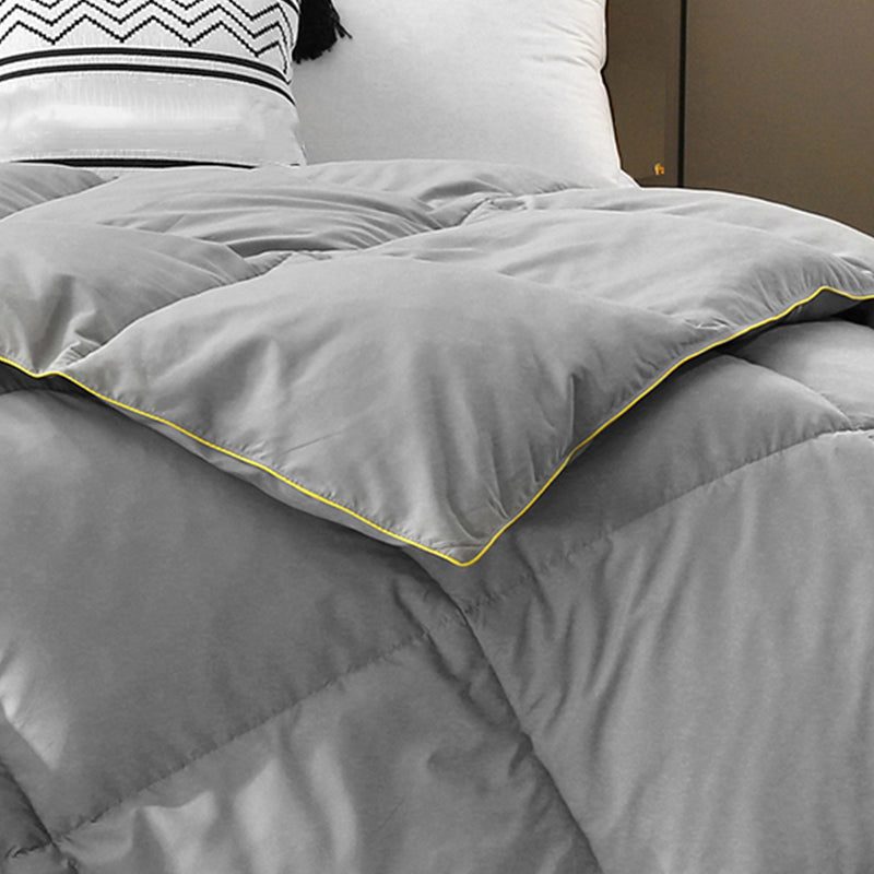 Close-up of a gray down comforter with yellow trim on a made bed with decorative pillows.