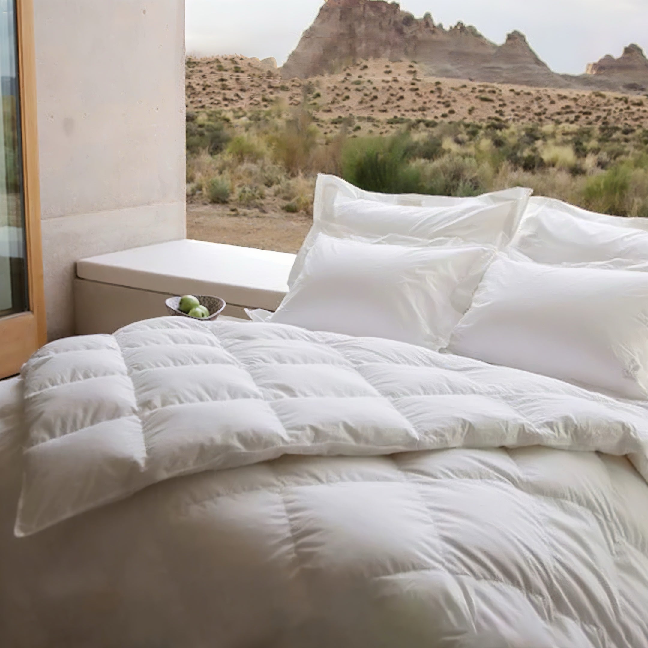 View of a bed with white linens on a patio with a desert landscape in the background.