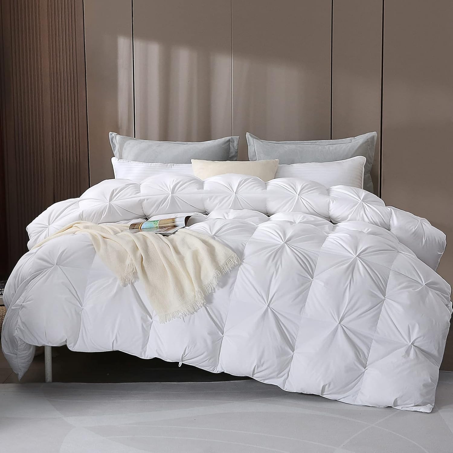 Close-up of a neatly made bed featuring APSMILE's Pinch Pleat duvet cover, showcasing its diamond-patterned stitching, topped with a folded cream-colored throw and a book, accompanied by soft grey pillows.