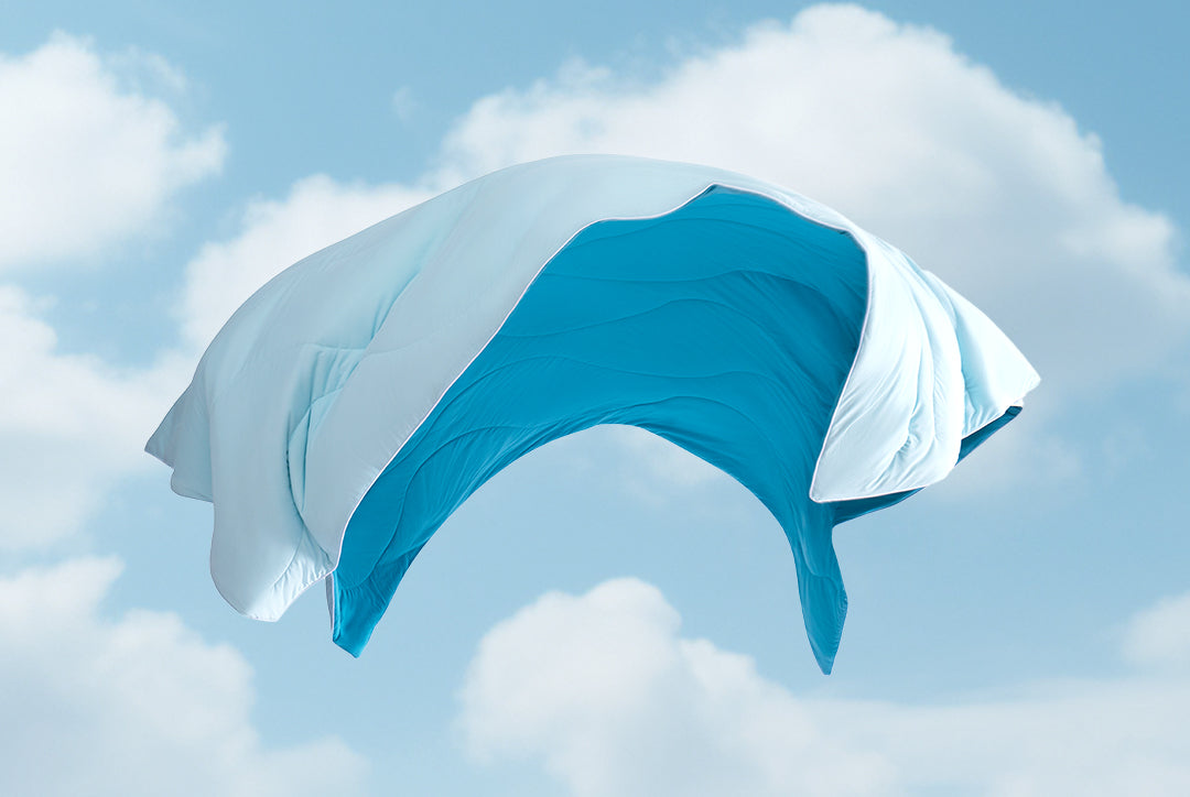 A light blue and teal comforter is suspended against a background of a light blue sky with scattered clouds.